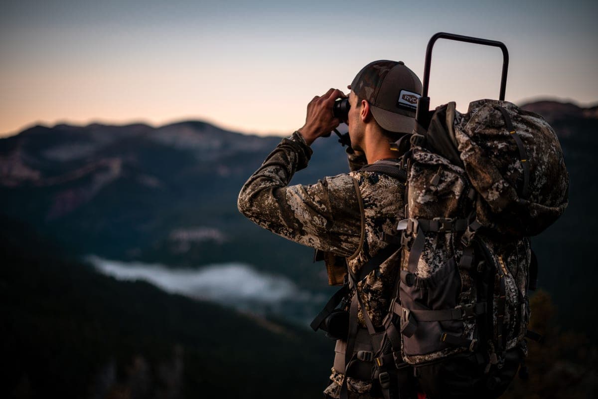 A person using binoculars on a hillside at dusk