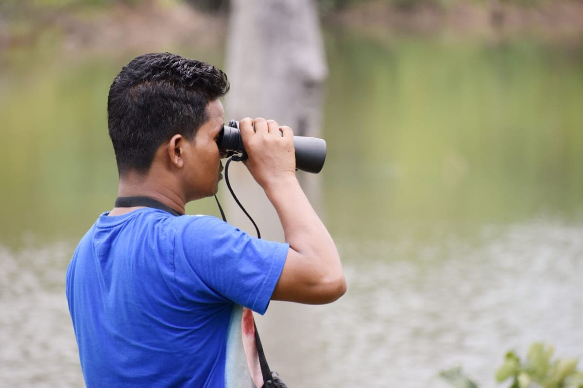 A person using binoculars beside a lake