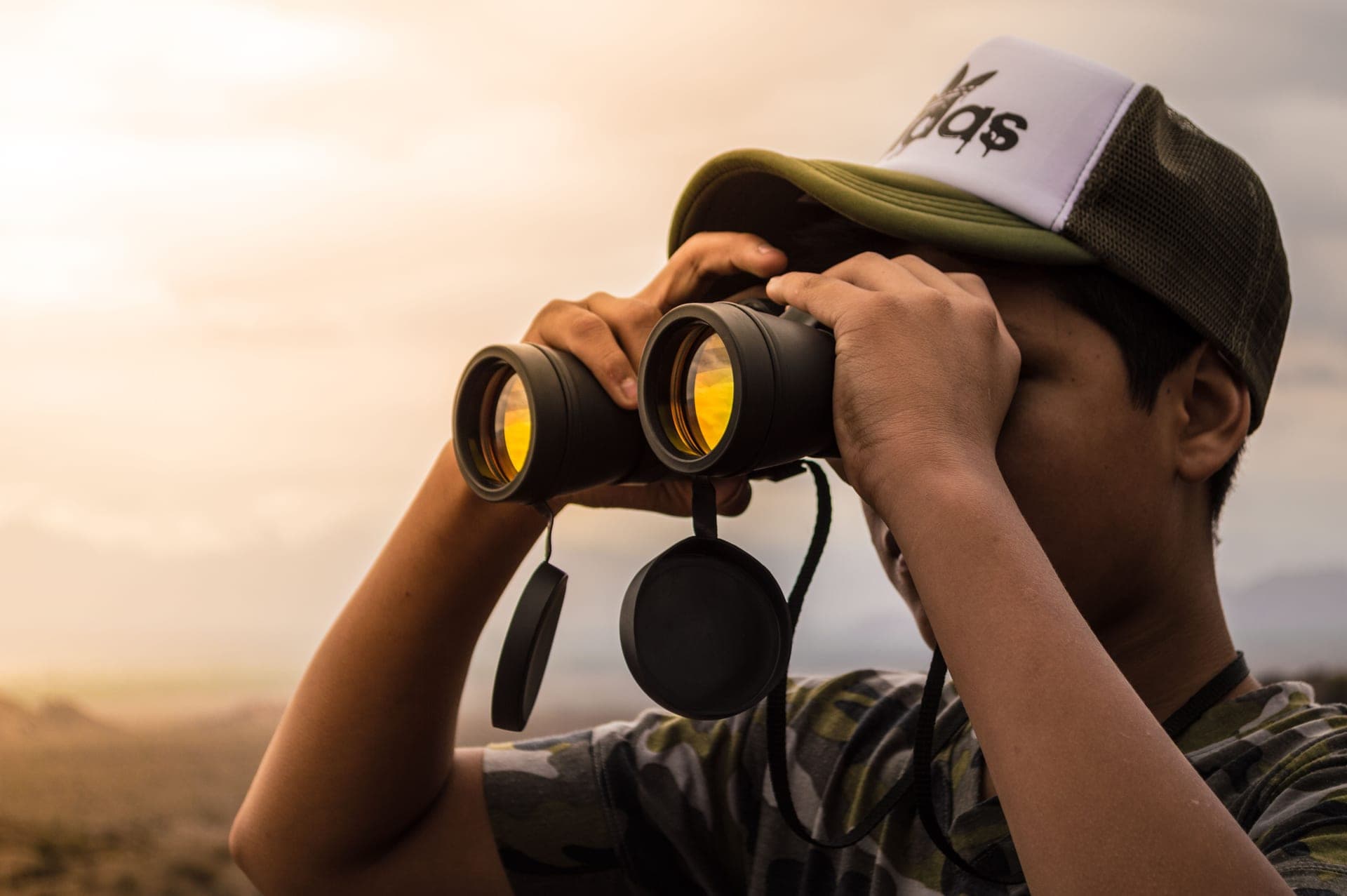 A young man using binoculars outdoors at golden hour