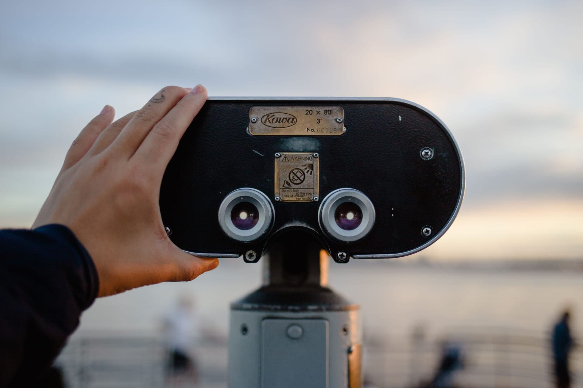 A hand adjusting a pair of large tripod-mounted viewing binoculars