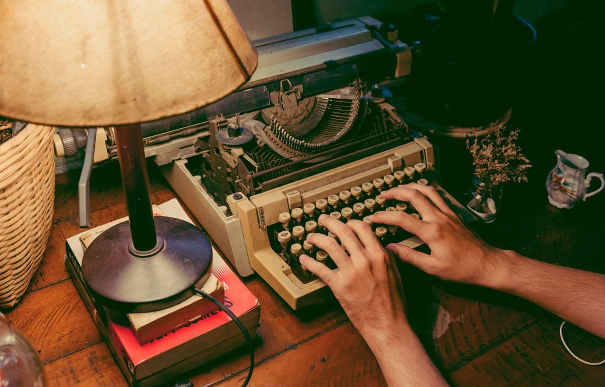 Hands typing on a typewriter under a warm lamp