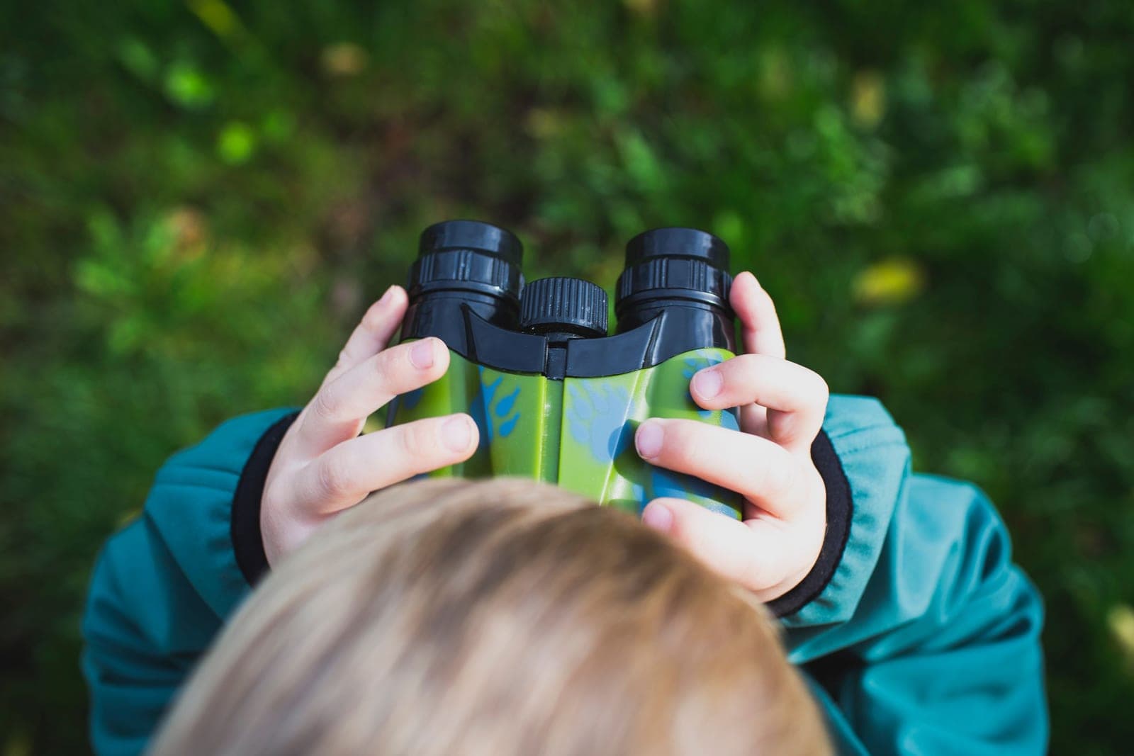A child holding binoculars up to their eyes outdoors