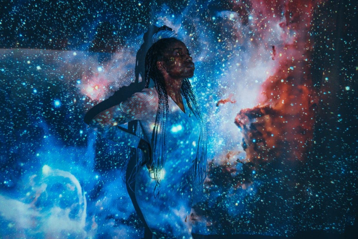 A person standing in a projected star field of blue and red nebulae