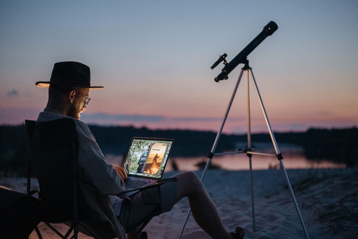 A telescope on a tripod beside a lake at sunset