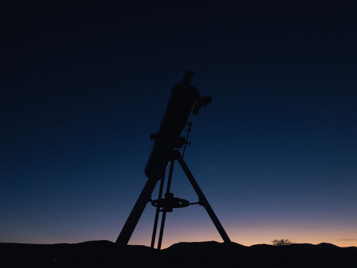 A refractor telescope on a tripod outdoors at dusk