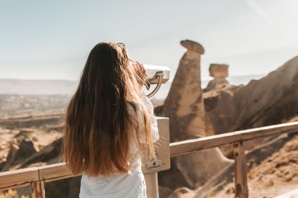 A young person looking through a mounted telescope at a landscape