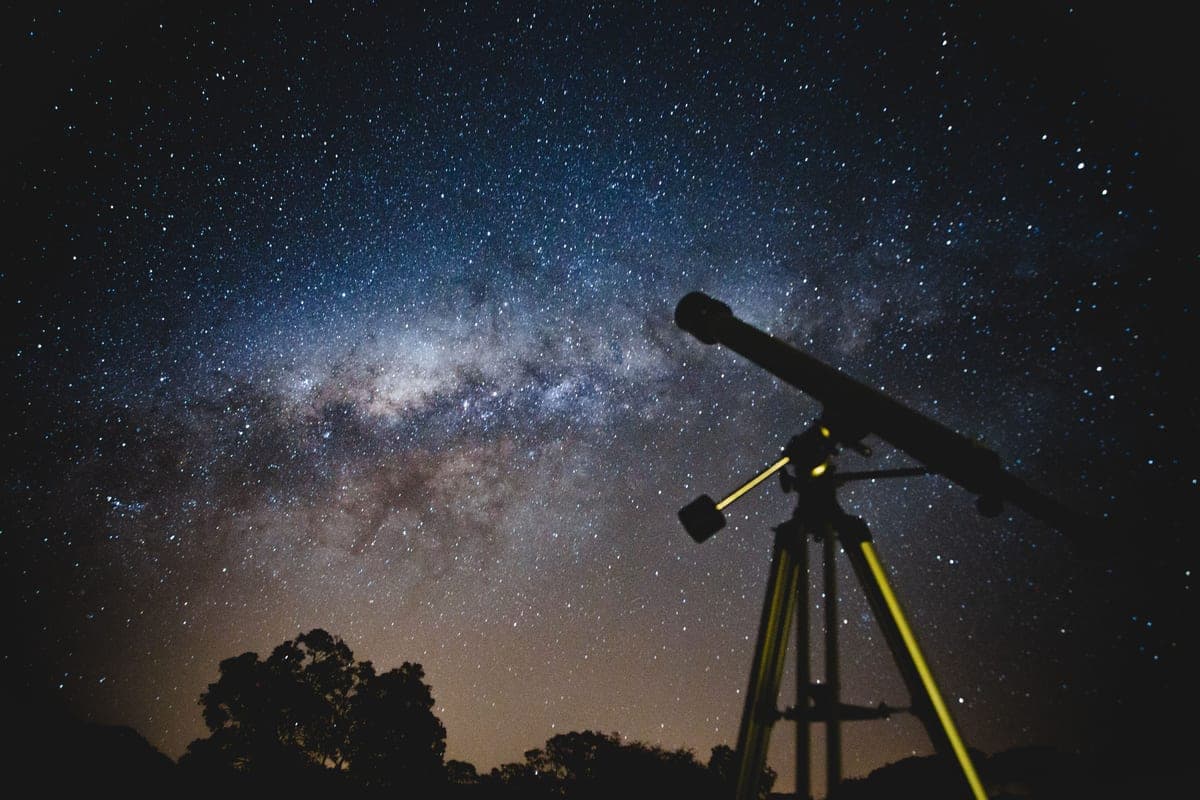 A large reflecting telescope silhouetted against a starry night sky