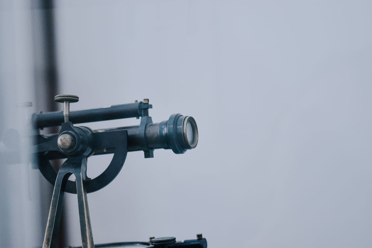 A vintage telescope on a mount with a graduated arc, against a pale gray background