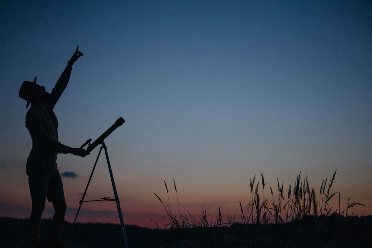 A reflecting telescope standing on a table outdoors under a night sky