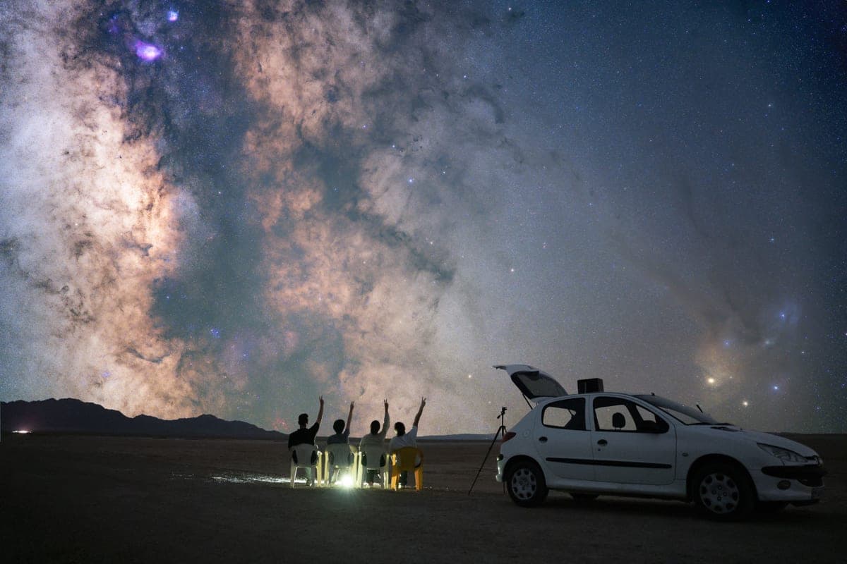Stargazers under the Milky Way, one holding up a phone to the sky