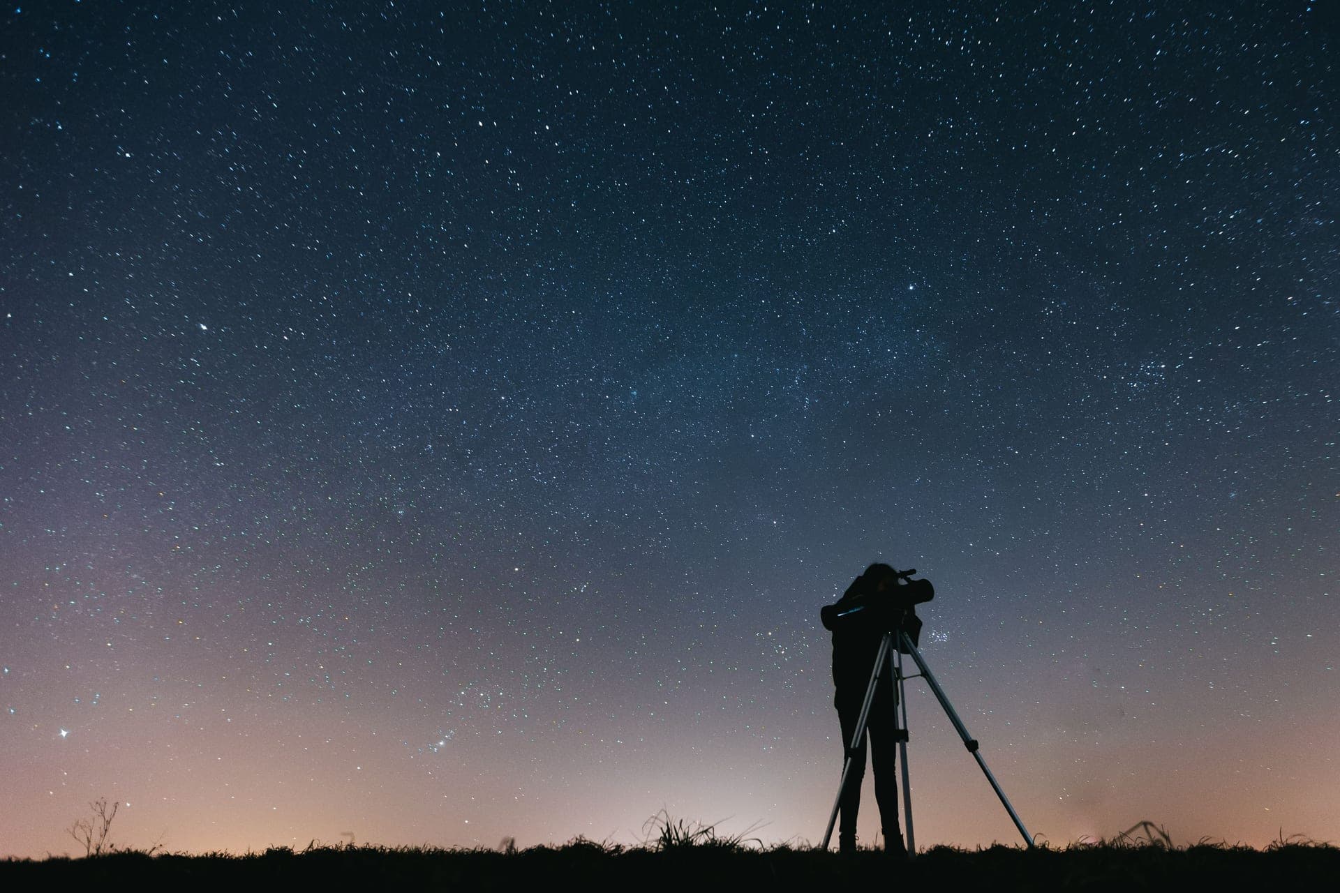 A silhouetted figure at a telescope under a star-filled sky